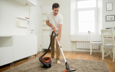Man cleaning carpet with vacuum in well-lit room, showcasing professional carpet cleaning techniques related to All Seasons Carpet Cleaning services.