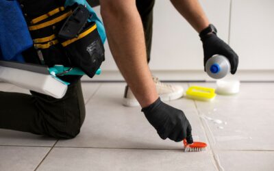 Professional cleaner using a brush and cleaning solution to scrub grout on tiled floor, showcasing effective tile and grout cleaning techniques.