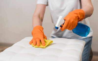 Person in orange gloves cleaning a mattress with a spray bottle and yellow cloth, illustrating steps for removing stains from mattresses.