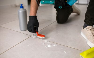Person cleaning tile floor with brush and cleaning solution, emphasizing tile and grout maintenance for a healthier home environment.