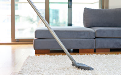 Vacuum cleaner nozzle on plush white carpet in a modern living room with gray couch, emphasizing carpet cleaning for improved air quality.