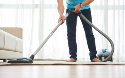 Man vacuuming carpet in a bright living room, emphasizing carpet cleaning services relevant to All Seasons Carpet Cleaning.