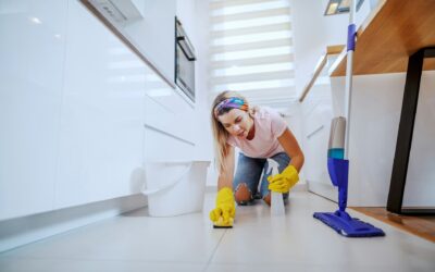Woman wearing yellow cleaning gloves, kneeling on kitchen floor, scrubbing tiles with a sponge, showcasing home cleaning practices relevant to maintaining cleanliness and hygiene.