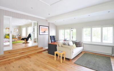 Bright and inviting living room with a beige sofa, wooden flooring, and large windows, showcasing a clean and organized space ideal for carpet and upholstery care tips.