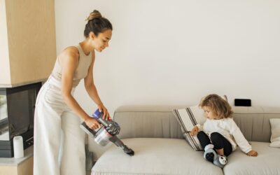 Woman using a vacuum cleaner on a couch while a child sits nearby, illustrating the importance of professional couch cleaning for family comfort and hygiene.