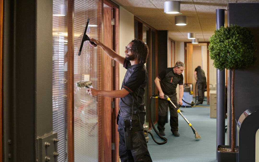 Workers cleaning office space with window squeegee and carpet extractor, emphasizing professional cleaning services for commercial environments.