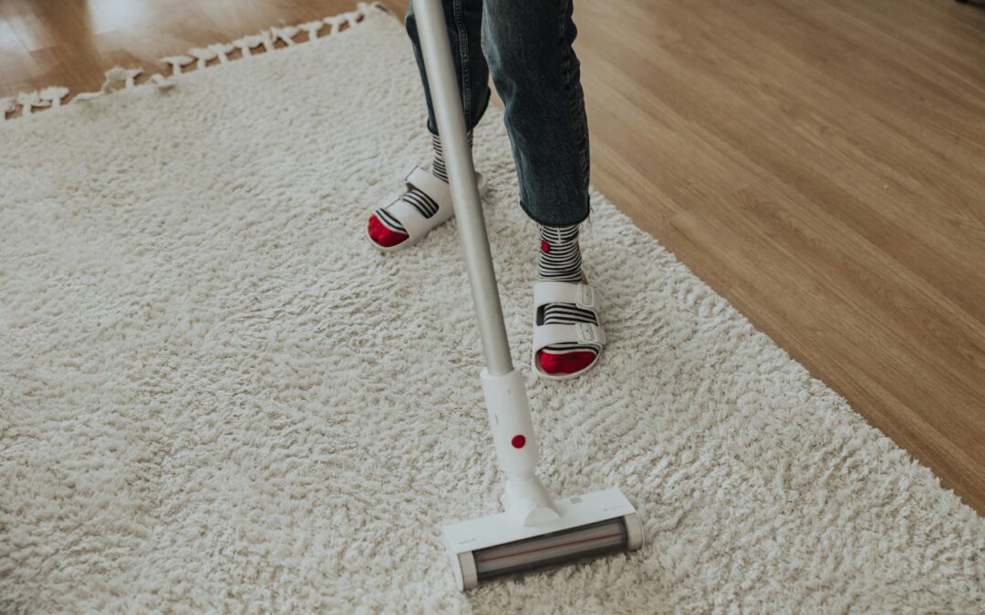 Person using a vacuum cleaner on a fluffy white area rug in a cozy home setting, emphasizing seasonal rug maintenance and cleanliness.